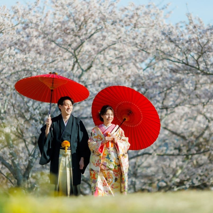 桜をバックに赤い傘を持った新郎新婦