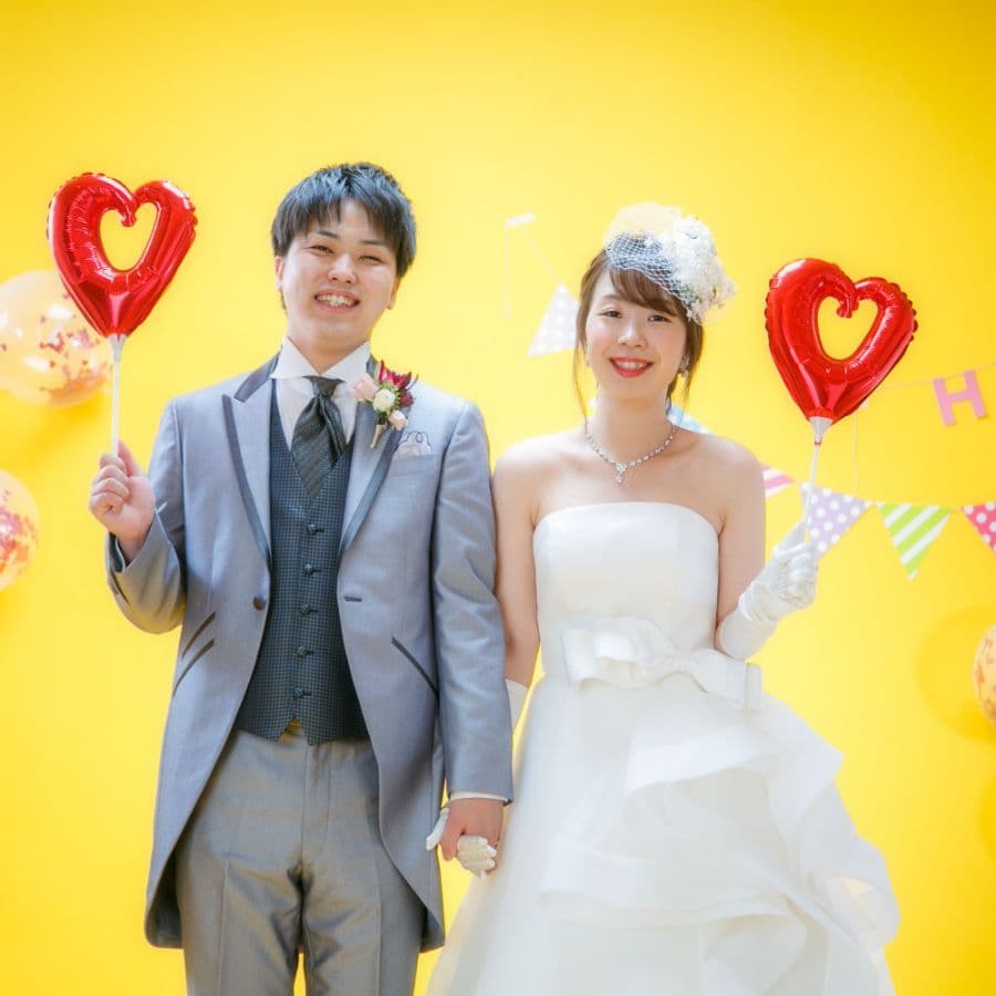 黄色バックにハートを持った新郎新婦