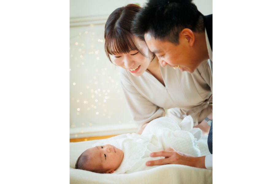 赤ちゃんをパパとママが上から笑顔で見つめている