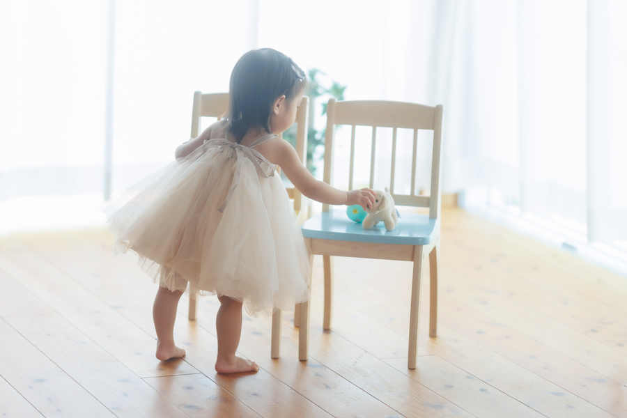 1歳バースデー女の子　後ろ向きで椅子の上の人形を触っている