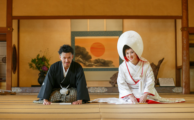 賓日館大広間にて 日の丸の掛け軸をバックに正座してお辞儀する新郎新婦