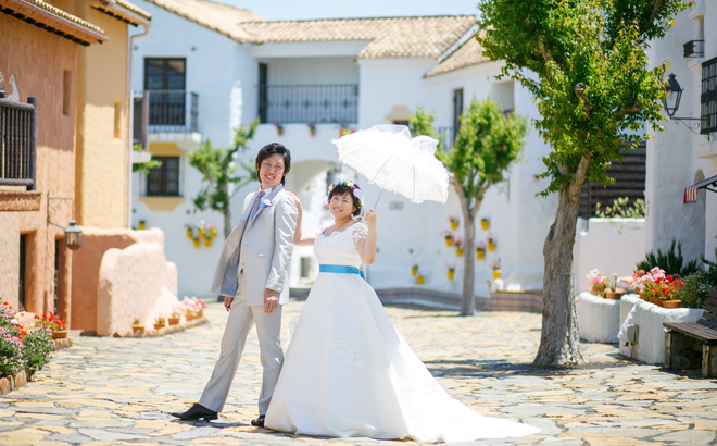 志摩地中海村 街並みの中で ウェディングドレスとタキシードの新婦と新郎 新婦は白い傘をさしている