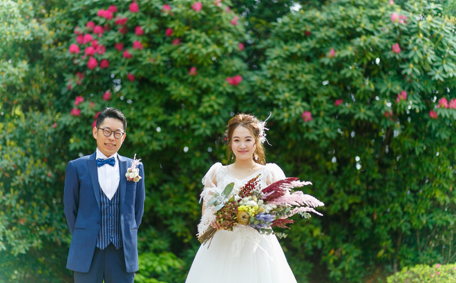 鳥羽国際ホテル チャペル前にて 新郎青いタキシード 新婦白ドレス ピンクの花が咲くグリーンの前で