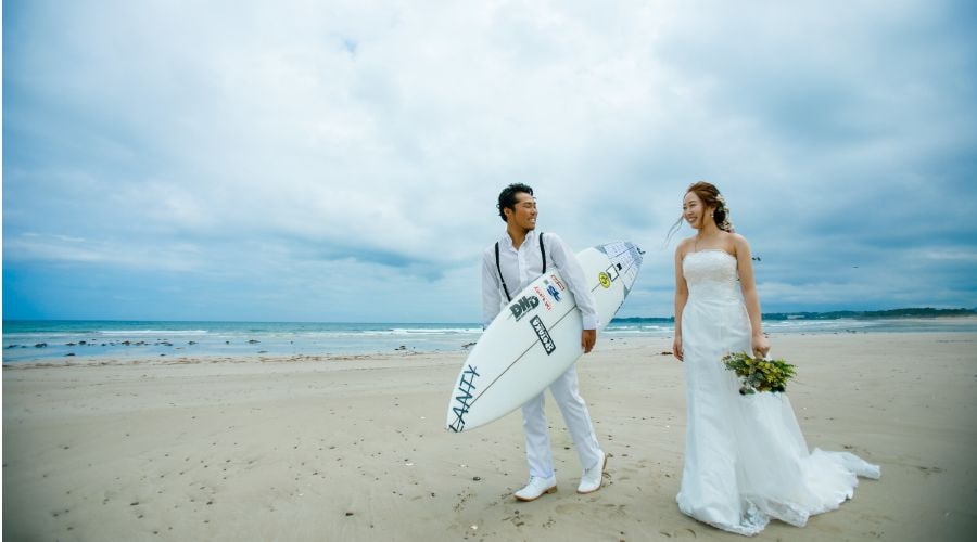 志摩市　国府海岸にて　新郎がサーフボードを持って　新婦と二人で歩いている