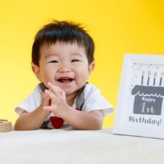 1歳男の子　1歳記念の額を隣において　拍手して笑顔