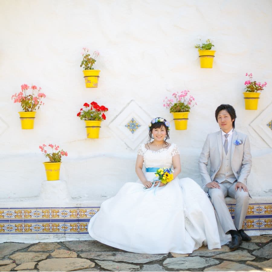 志摩地中海村にて新郎新婦撮影。鉢植えの花が飾られた壁の前で