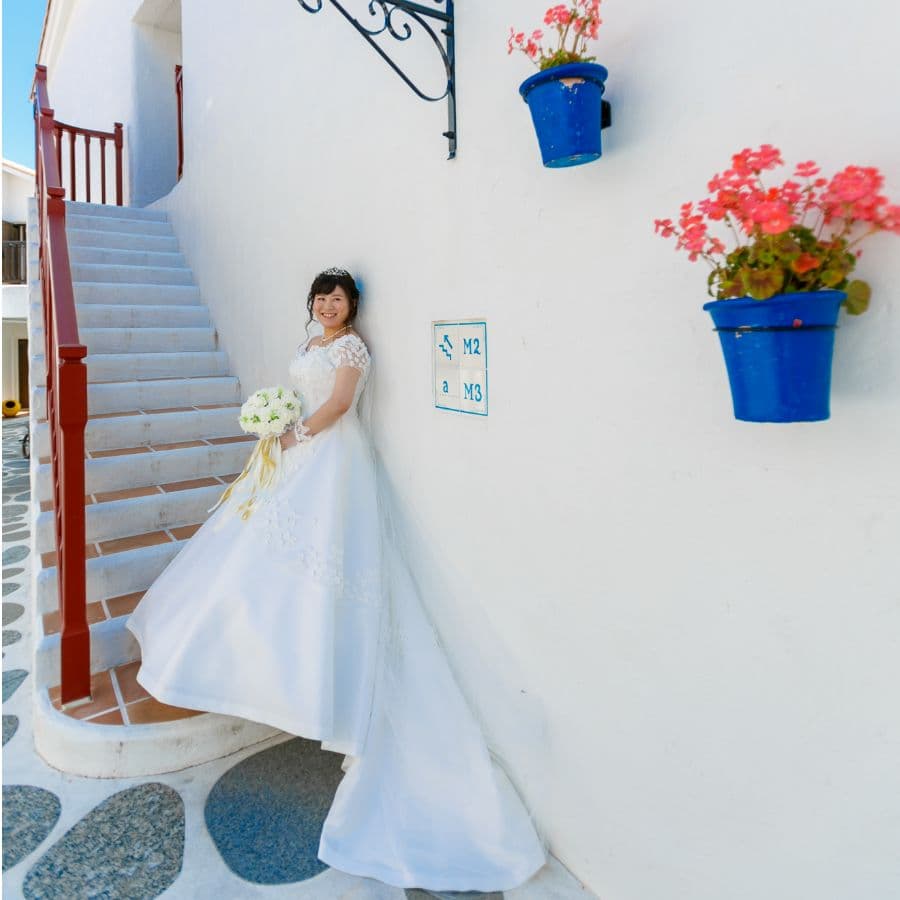 志摩地中海村にて新婦1人白ドレス撮影。鉢植えの花が飾られた壁の前で