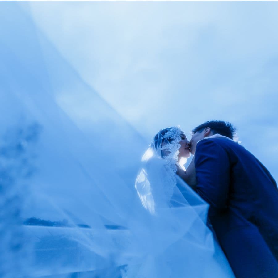 志摩地中海村にて新郎新婦撮影。ベールが吹き上がる中でキスをする新郎新婦